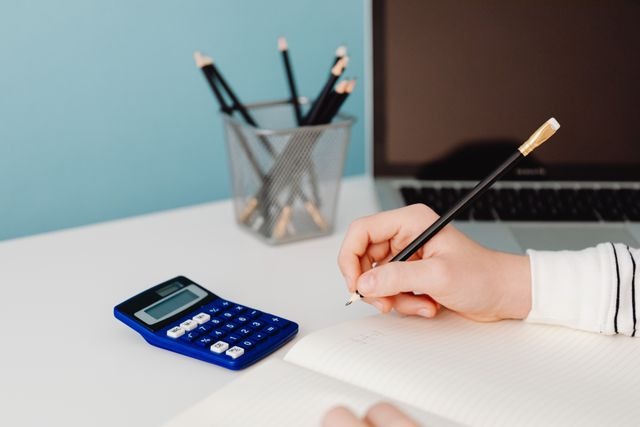 person writing next to a blue calculator
