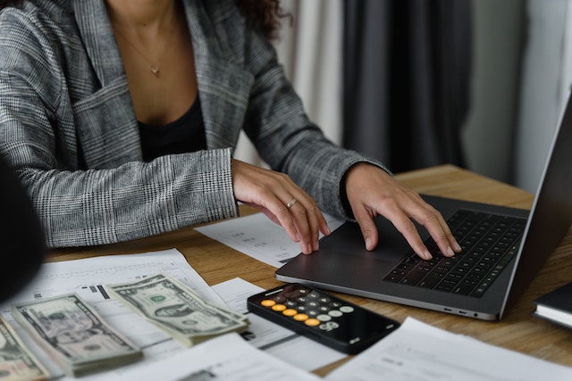 an accountant working on their laptop with stacks of cash next to them