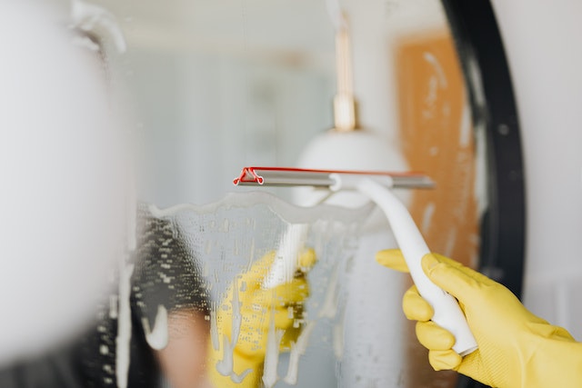 hand wearing yellow gloves while cleaning a mirror