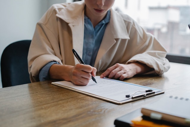 person in a blue shirt and beige coat filling out a questionnaire